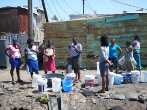 Residents waiting to fill their water buckets and basins at communal tap. 